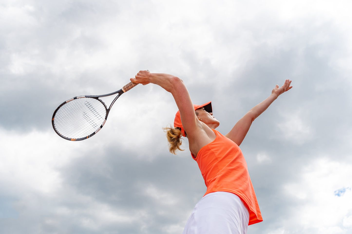 woman looks to spike a tennis ball on a bright and cloudy day