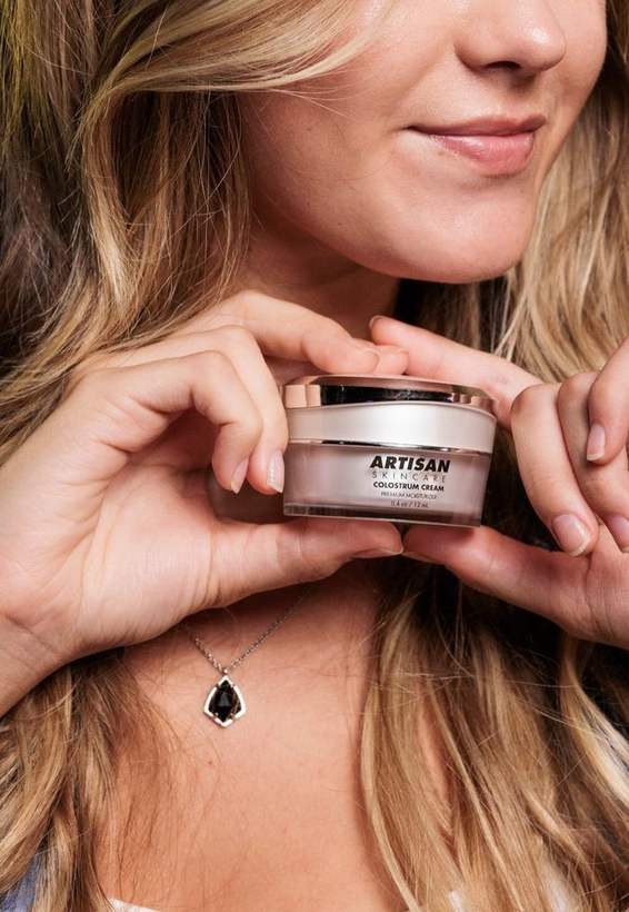 A woman holding the Artisan The Goat Colostrum Cream jar against her collarbone.